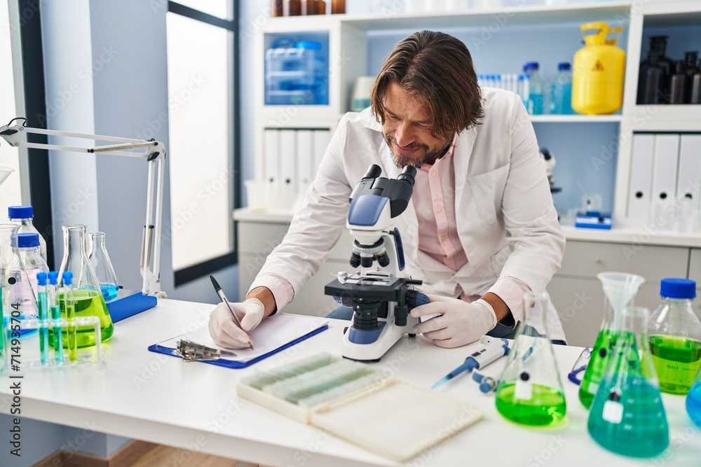 Middle age man scientist using microscope writing on document at laboratory Middle age man scientist using microscope writing on document at laboratory