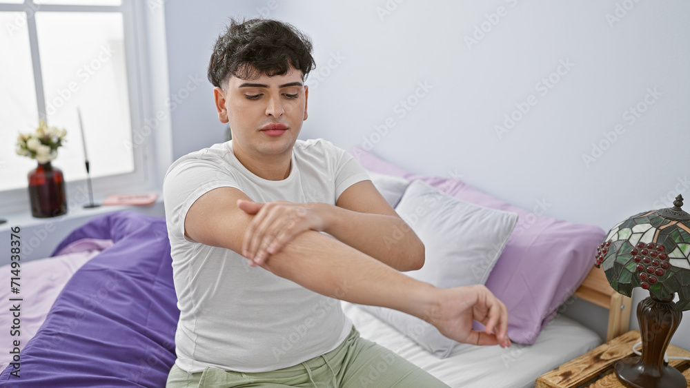 Young man applying lotion on his arm sitting on a bed in a bright bedroom Young man applying lotion on his arm sitting on a bed in a bright bedroom