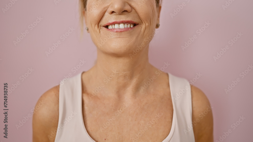 A smiling middle-aged woman with blonde hair against a pink isolated background portraying positivity. A smiling middle-aged woman with blonde hair against a pink isolated background portraying positivity.