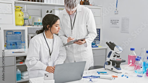 A woman and man  seemingly coworkers  analyze data together on a laptop in a well-equipped laboratory setting.