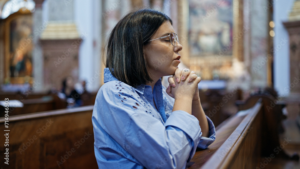 Fototapeta premium Young beautiful hispanic woman praying on a church bench at St. Karl BorromÃ¤us church