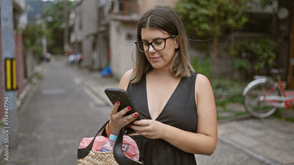 Beautiful young hispanic woman enjoying kyoto's city streets, happily texting with joy on smartphone, sporting glasses and confident smile! Beautiful young hispanic woman enjoying kyoto's city streets, happily texting with joy on smartphone, sporting glasses and confident smile!