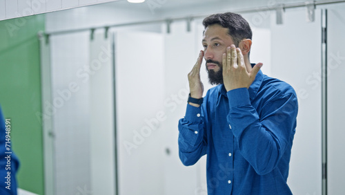 Young hispanic man washing face at bathroom