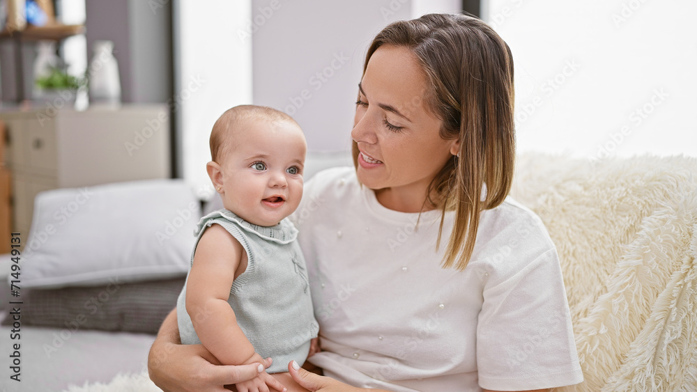 Mother's loving smile, engaged in joyful laughter while sitting together with daughter on sofa at home amidst casual indoor lifestyle Mother's loving smile, engaged in joyful laughter while sitting together with daughter on sofa at home amidst casual indoor lifestyle