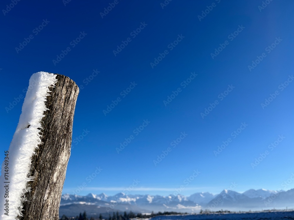 Closeup of wooden fence post with snow on one side, deep blue sky in the background Closeup of wooden fence post with snow on one side, deep blue sky in the background