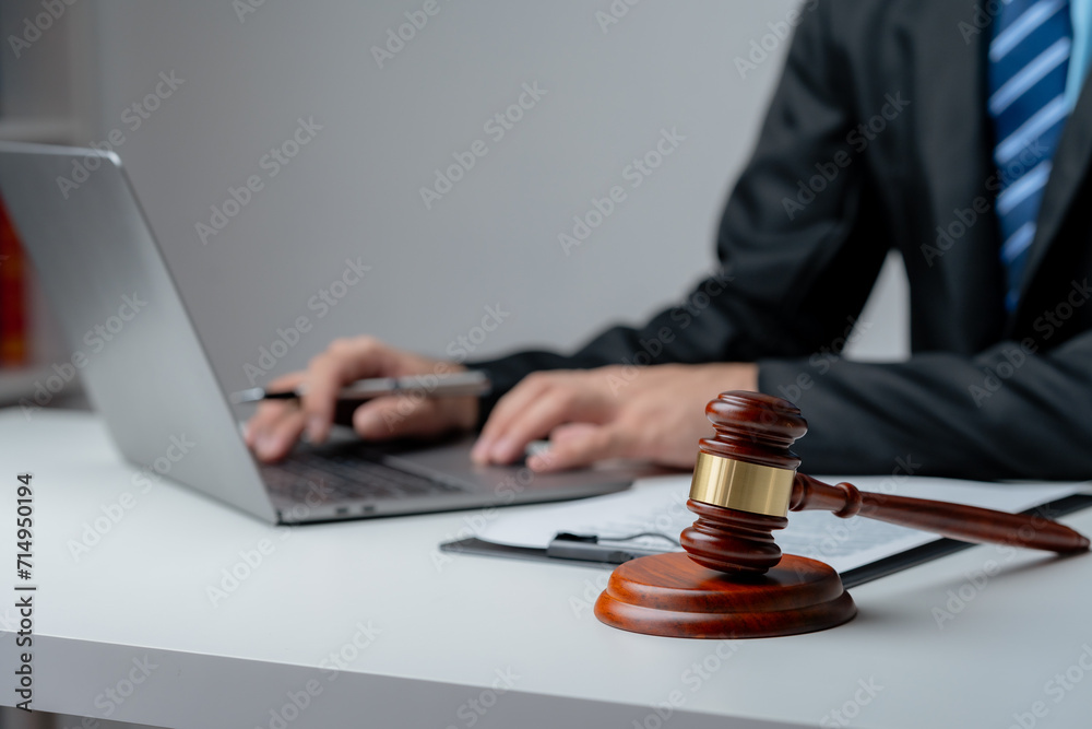 Legal professional in suit typing on a laptop with a judge's gavel in the foreground, symbolizing law and justice.. - obrazy, fototapety, plakaty 