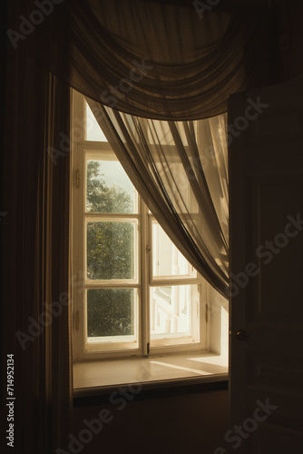 A picture of a window with the curtains ajar. Sunlight penetrates through the curtained window. How the windows were decorated at the end of the XIX century.