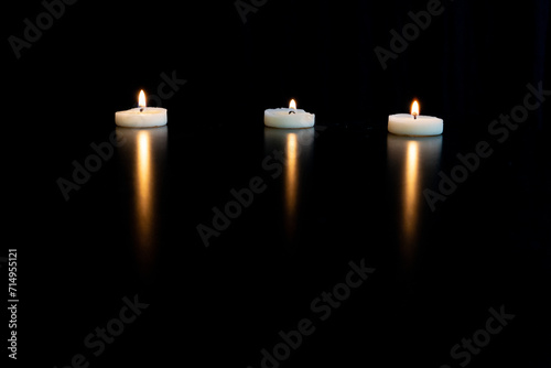 trois petites bougies blanches chauffe plat et leur reflet sur une table noire avec de l'espace vide