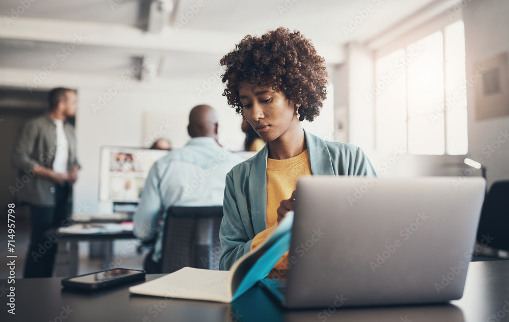 Young businesswoman working at her office desk with coworkers talking in the background Young businesswoman working at her office desk with coworkers talking in the background