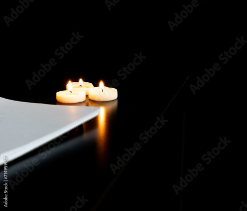 trois petite bougies regroupées allumées sur une table avec un fond noir et un coin de cahier vierge  photo