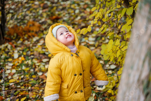 Little cute baby toddler child in a hat and yellow jacket, child in an autumn park outdoors