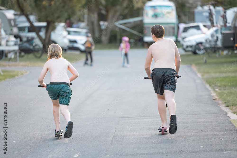 Kids riding scooters through caravan park on tropical holiday Kids riding scooters through caravan park on tropical holiday