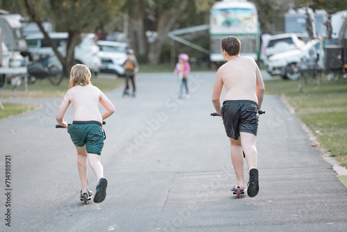 Kids riding scooters through caravan park on tropical holiday © Caseyjadew