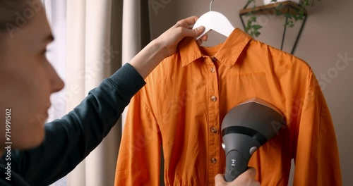 woman ironing shirt with electric clothes steamer at home photo