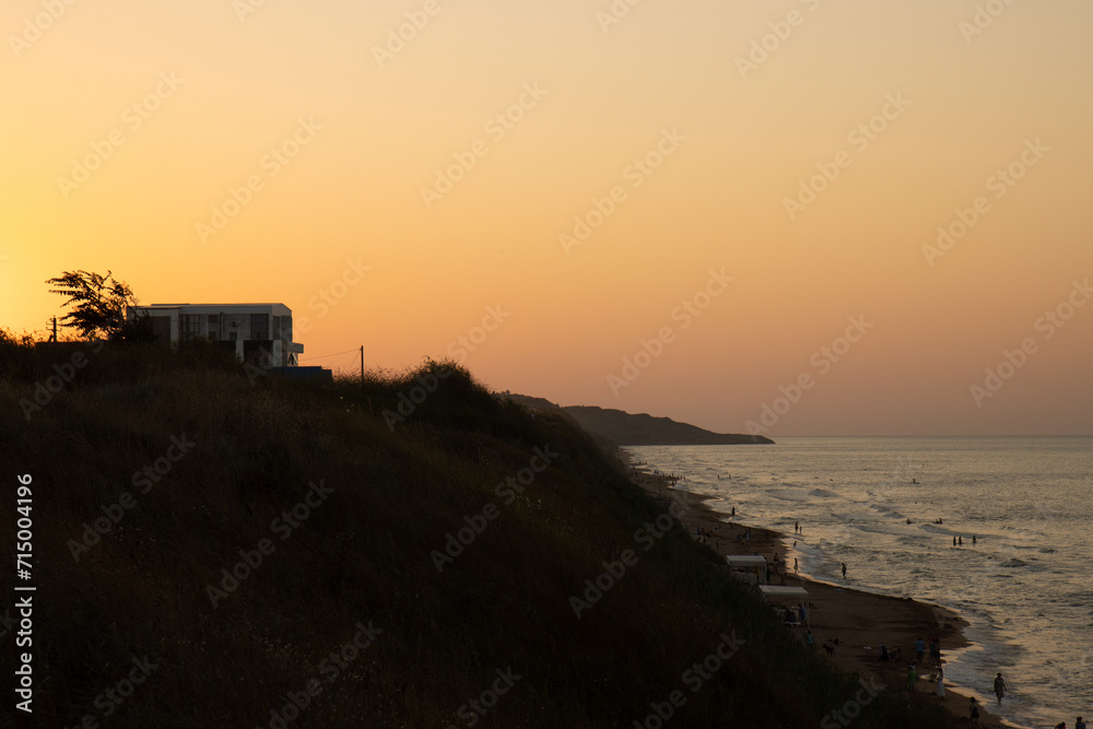A house by the sea. The setting sun illuminates the house by the sea. A summer house on a hill by the sea.