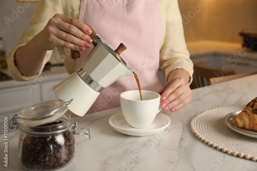 Woman pouring aromatic coffee from moka pot into cup at white marble table  closeup