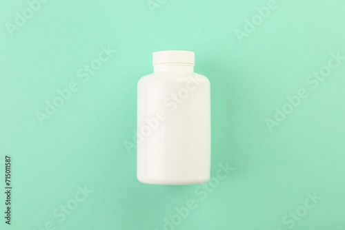 Blank white pill bottle on turquoise background, top view. Space for text