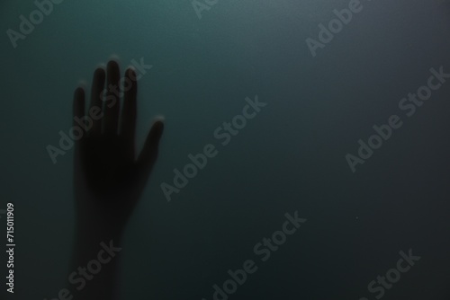 Silhouette of creepy ghost behind glass against color background, closeup. Space for text