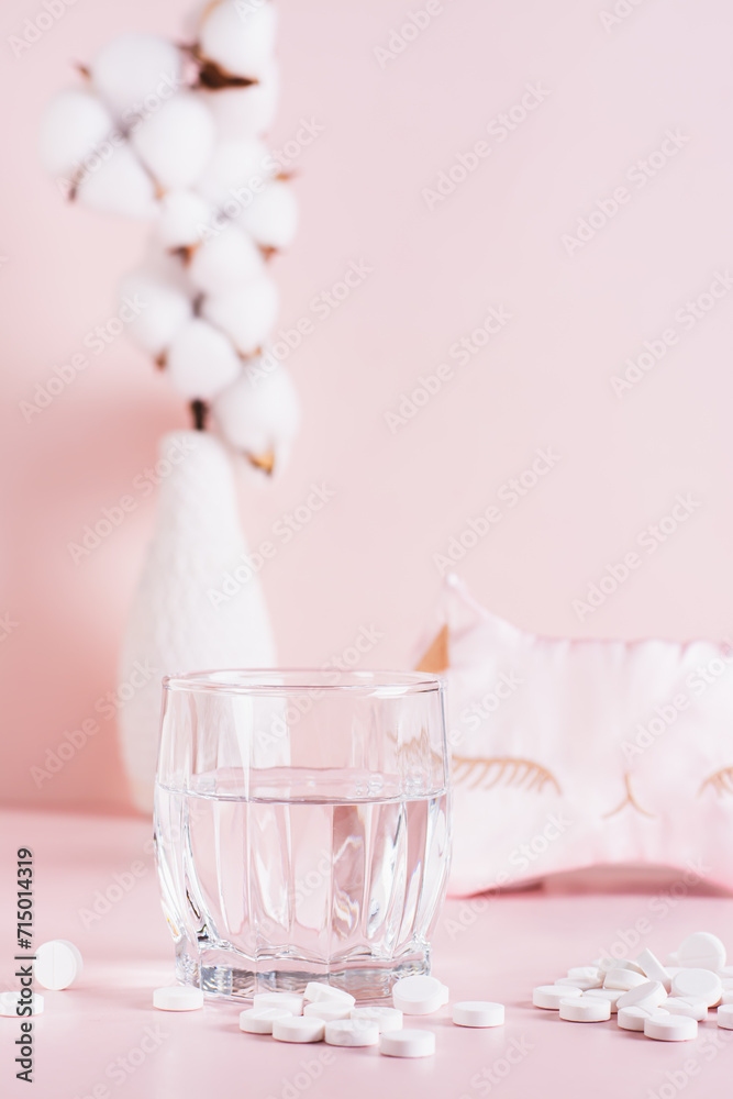 Sleeping pills, a glass of water and a sleep mask on a pink background vertical view Sleeping pills, a glass of water and a sleep mask on a pink background vertical view
