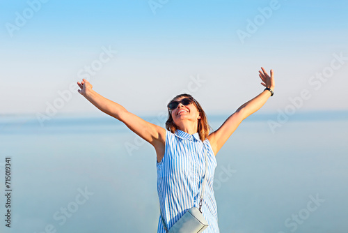Happy young brunette woman open her arms to the sky and sea