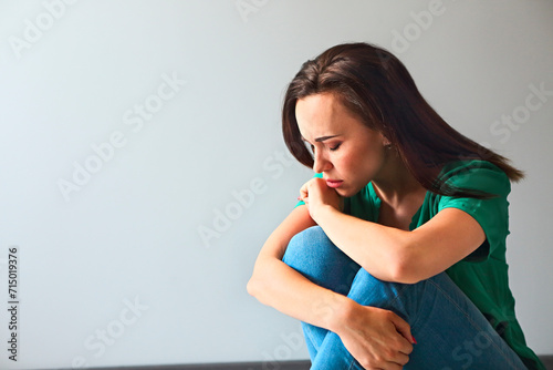 Sad woman looking thoughtful about her troubles in front of a gray wall