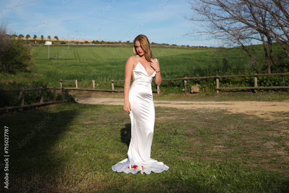 A beautiful young woman, blonde and with long hair, wearing a white dress and a crown of flowers in her hair, is in a field. In the background a green wheat field. The woman is in different poses. A beautiful young woman, blonde and with long hair, wearing a white dress and a crown of flowers in her hair, is in a field. In the background a green wheat field. The woman is in different poses.