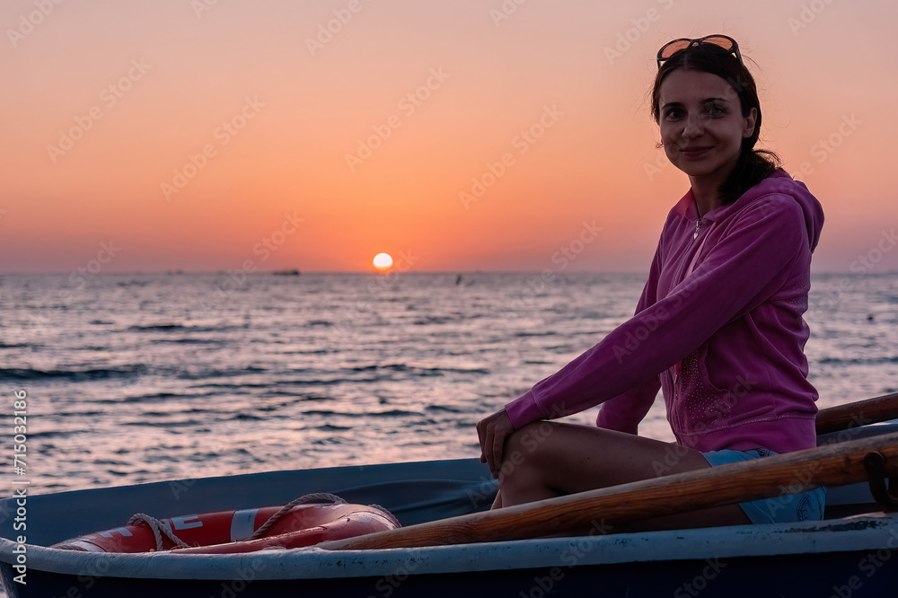 Woman sitting in boat in sea against the background of sunset Woman sitting in boat in sea against the background of sunset
