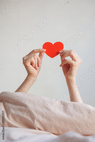 women's hands holding red heart shaped postcard, surprise gift for Valentine's day. February 14th is holiday of love happiness. tradition in relationship, date. surprise greeting for the day of love.