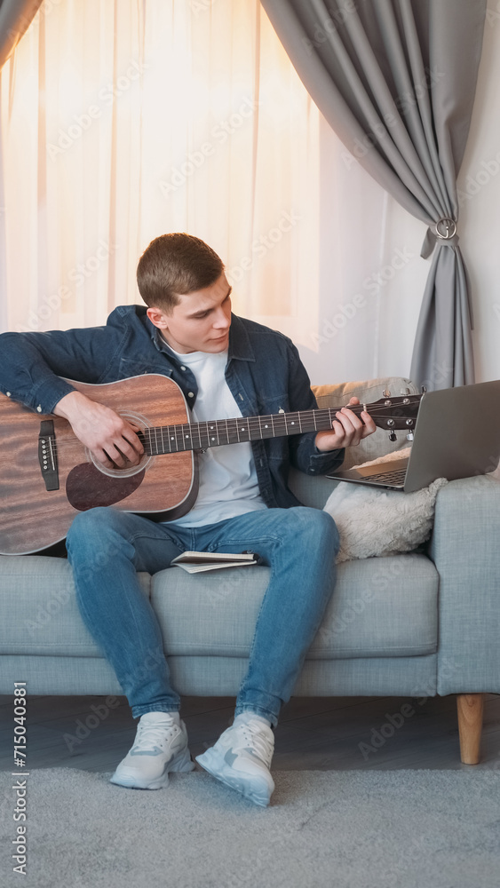 Obraz premium Guitar course. Internet music class. Creative hobby. Inspired man learning string instrument chords lesson online at laptop on couch at home.