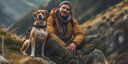 A man in hiking clothes resting from hiking in great outdoors landscape with a dog, with mountains behind © Tetyana