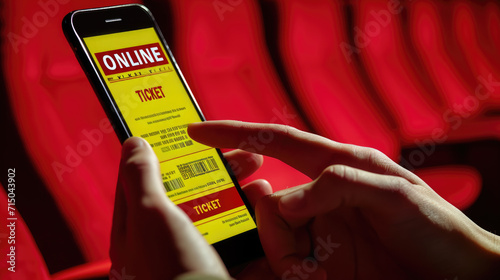 Person's hand holding a smartphone with a digital online ticket on the screen, with a blurred background featuring red theater or cinema seats. photo
