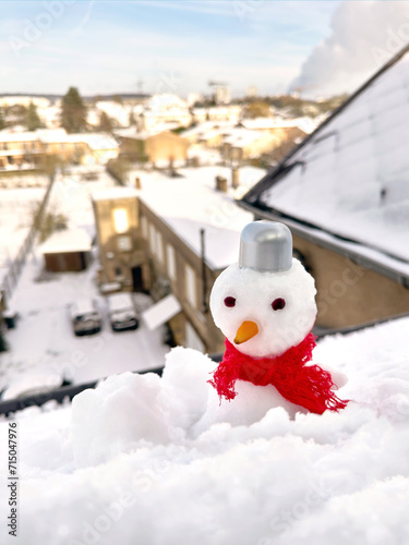 Small snowman in a red scarf against the backdrop of a winter city