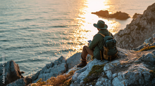 Traveler is sitting on a rocky cliff, reading a book with a serene sunset over the sea in the background