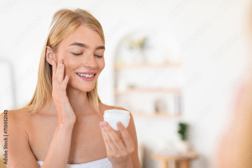 blonde woman applies facial cream embracing domestic skincare routine indoor