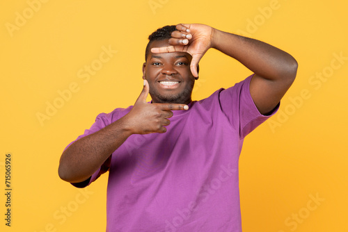 Cheerful african american guy making picture frame with fingers, studio