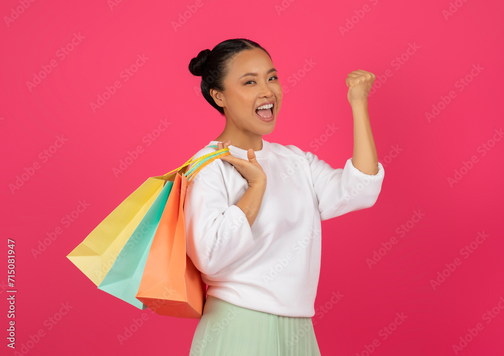 Big Discounts. Happy young asian woman carrying shopping bags and shaking fist Big Discounts. Happy young asian woman carrying shopping bags and shaking fist