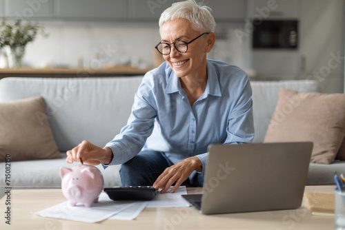 woman with piggybank putting coin managing funds near laptop indoor photo