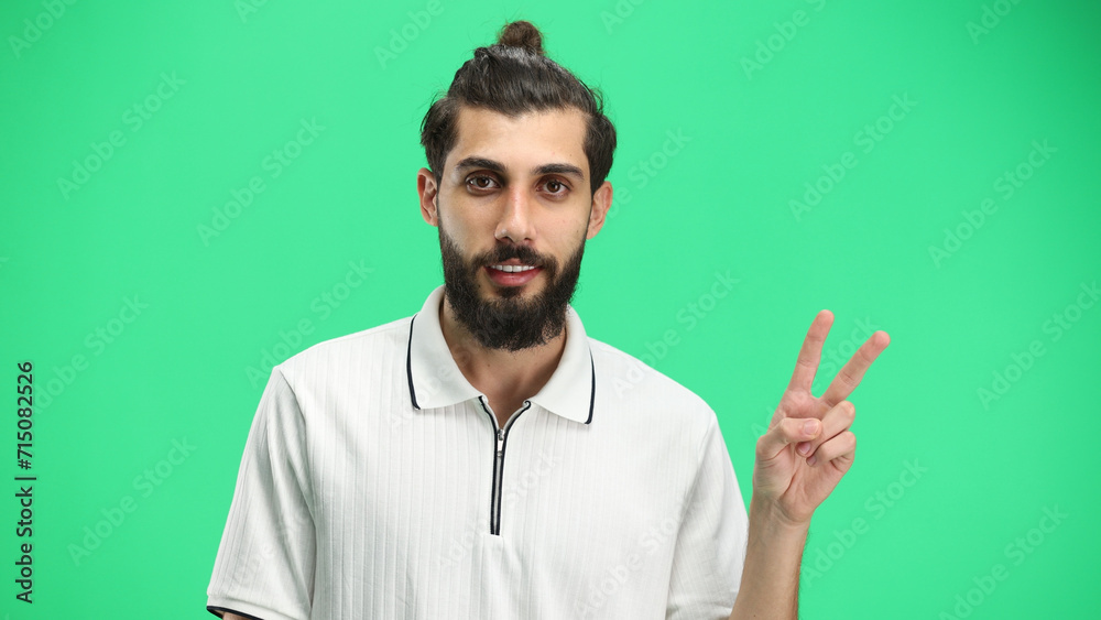 Naklejka premium A man, close-up, on a green background, shows a victory sign