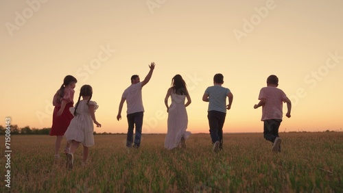 Family with children runs through grassy field in evening at sunset. Big family, group of people in nature. Parental care for children. Son, Daughter, dad, mom, walk, running outdoors. Holiday family