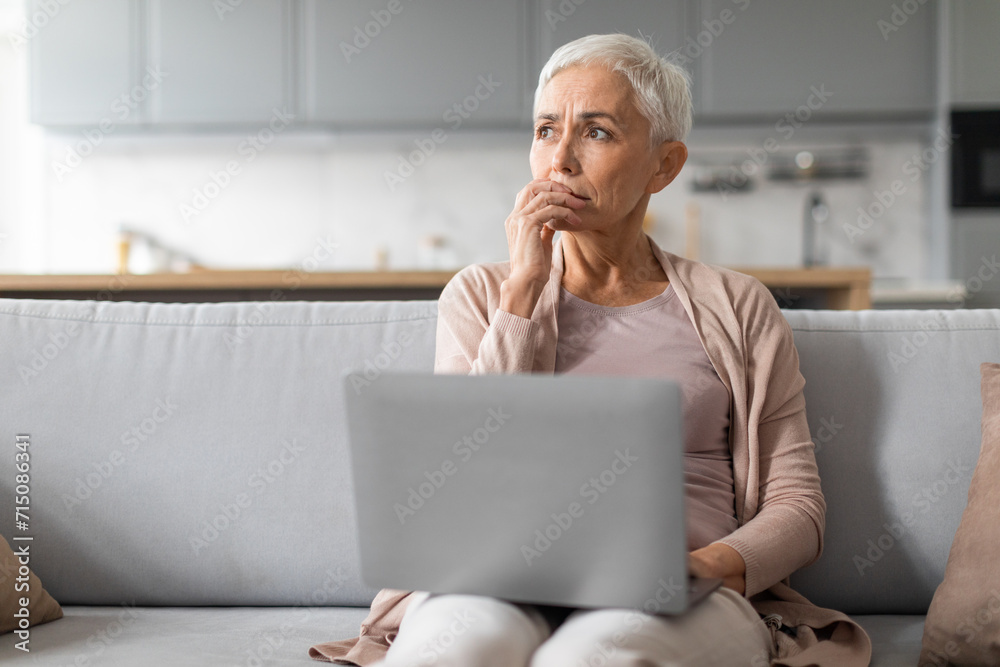 Concerned mature lady working on laptop thinking about issues indoor