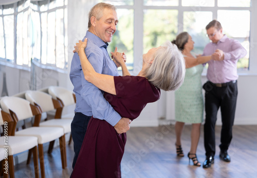 Pairs of mature amateur dancers enthusiastically performs romantic tango dance in modern dance salon photo