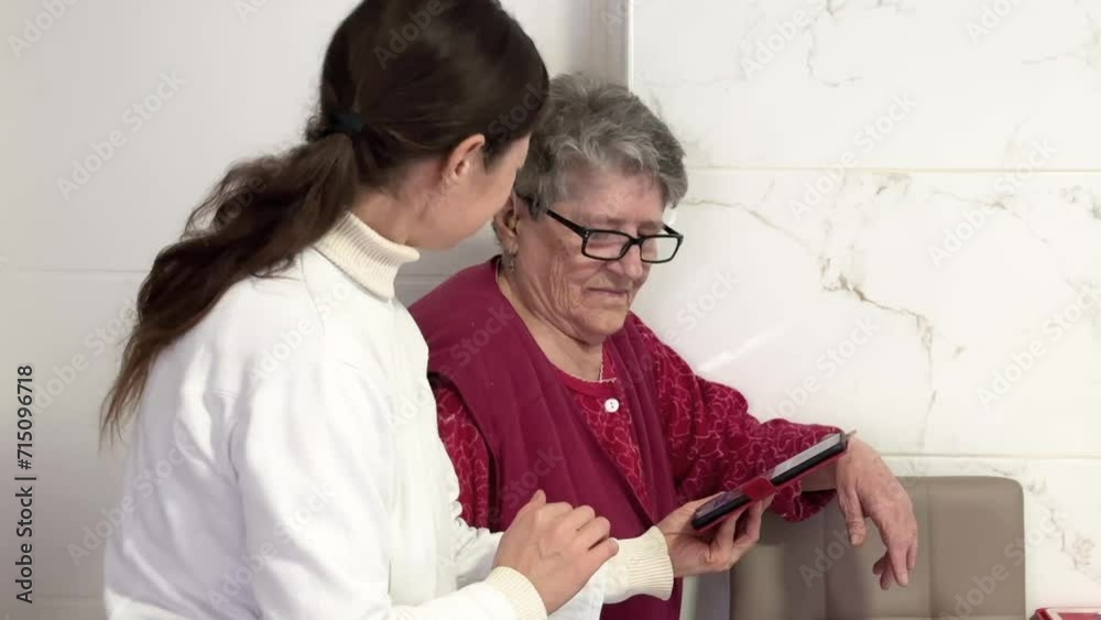 A middle-aged women explains the settings on a cell phone to an elderly grandmother. Learning new tenology by old people. Old people studying a cell phone with. Social worker helps old man A middle-aged women explains the settings on a cell phone to an elderly grandmother. Learning new tenology by old people. Old people studying a cell phone with. Social worker helps old man