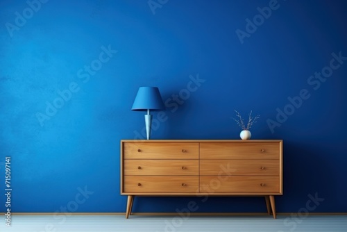  an empty room with a blue wall and a wooden dresser with a blue lampshade on top of it. photo