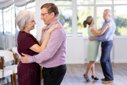 Smiling couple looking at each other while dancing slow dance in modern ballroom photo
