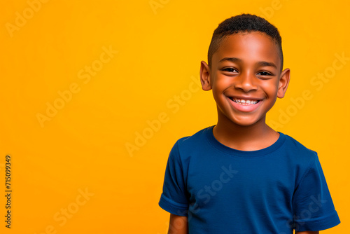 Portrait of a smiling African little boy in a blue t-shirt on yellow background. Front view, happy child in a blue shirt.