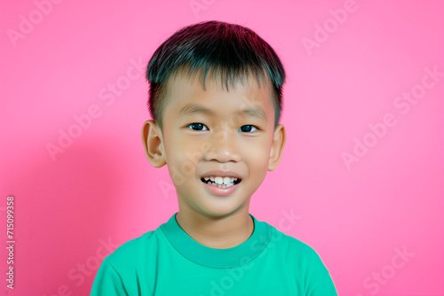 Portrait of a smiling Asian little boy in a t-shirt on pinkbackground. Front view, happy child in a blue shirt.