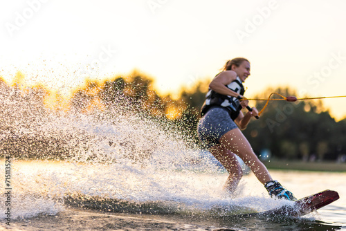 Female wakeboarder wakesurfing on sunset. Girl riding waterski cabel. Holding tow rope. Summer activities in the lake.