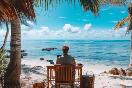A man escapes the hustle and bustle of daily life by sitting at an outdoor desk on a tropical beach, surrounded by the soothing sounds of the ocean and swaying palm trees as he works on his laptop © Vladan