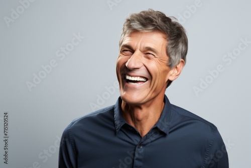 Handsome middle aged man laughing and looking at camera over grey background.