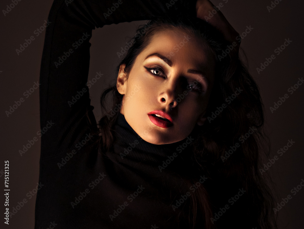 Beautiful makeup woman with red lipstick in black poloneck posing on dark shadow studio black background. Long brown hairstyle. Closeup Beautiful makeup woman with red lipstick in black poloneck posing on dark shadow studio black background. Long brown hairstyle. Closeup